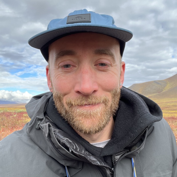 Selfie portrait of Alex in hat and coat standing in the tundra of the Brooks Range in fall.